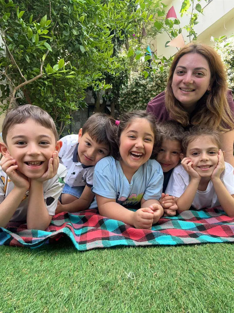 Bahçedeki piknik örtüsüne uzanmış gülen çocuklar ve öğretmenleri