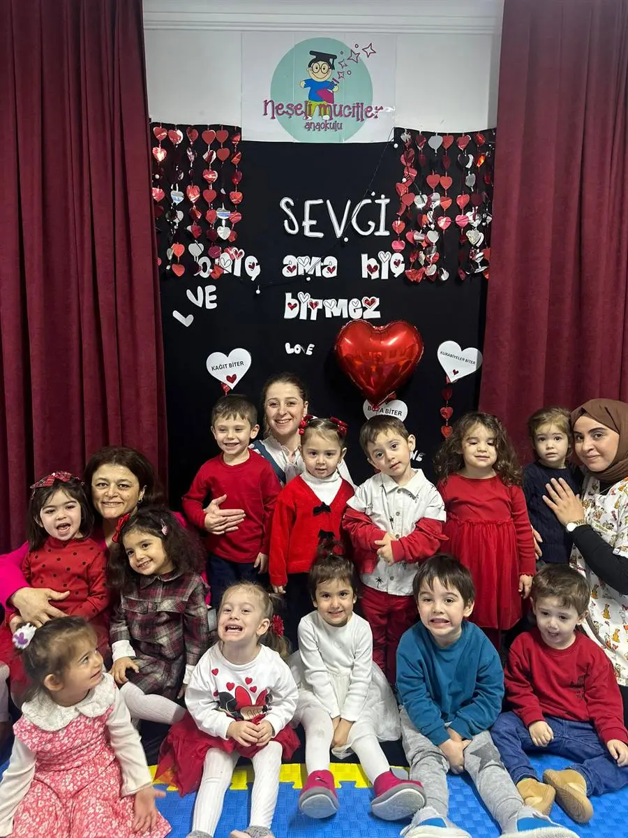 Kalp süslemeli pano önünde toplanan çocuklar ve öğretmenler