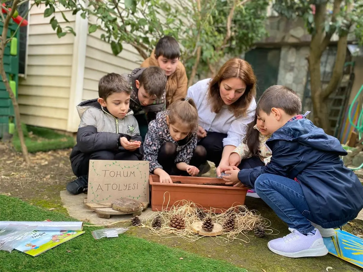 Bahçede saksıya tohum eken çocuklar ve onlara eşlik eden öğretmen